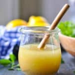 Front shot of lemon vinaigrette dressing in a glass jar with wooden spoon