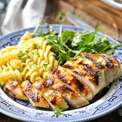 Front shot of grilled chicken breast on a plate with pasta and salad