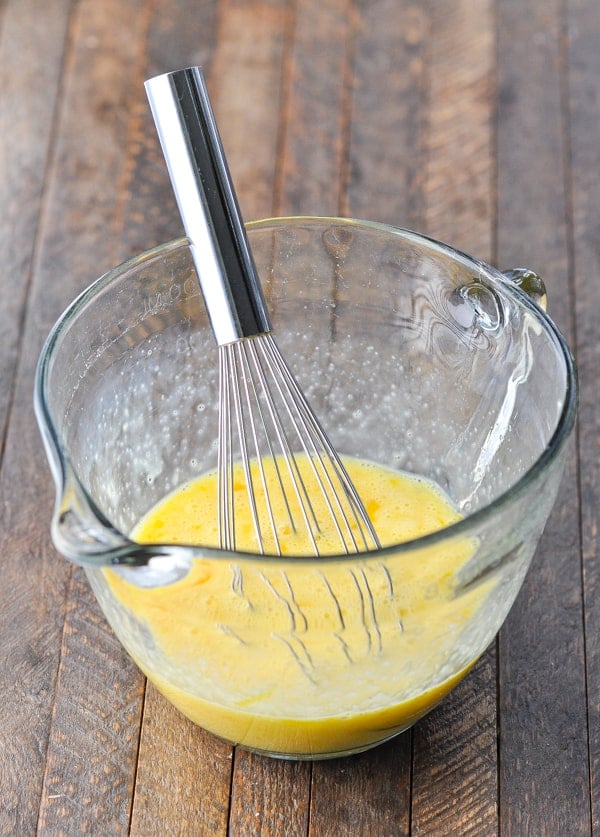Egg mixture for sausage hash brown casserole in a glass bowl with a whisk