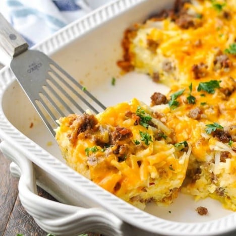 Front shot of sausage hash brown casserole in a white baking dish with a serving spatula