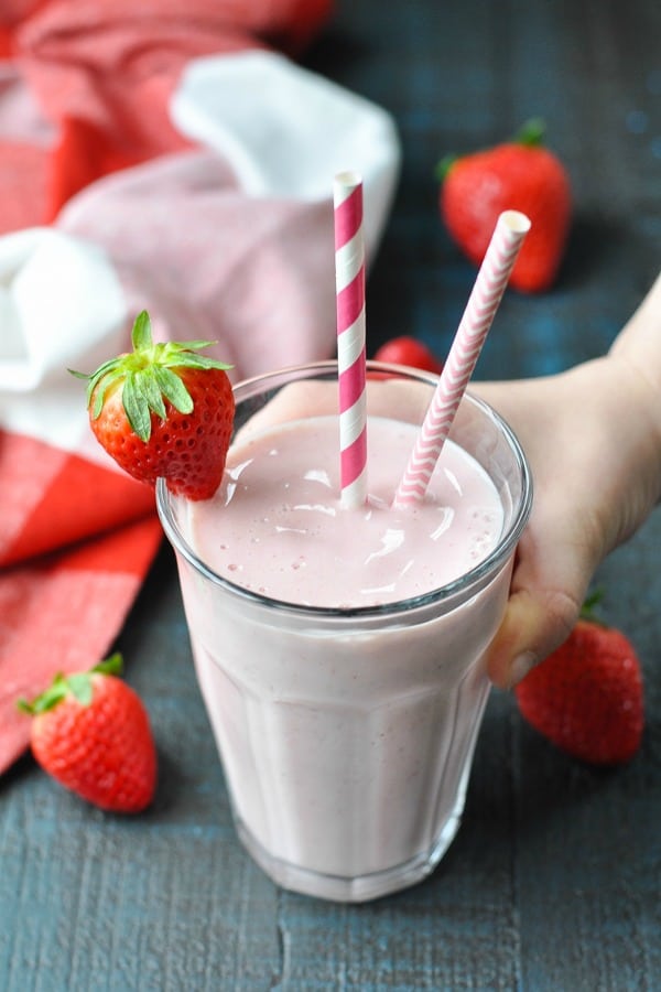 Child's hand picking up a glass of strawberry banana smoothie with yogurt