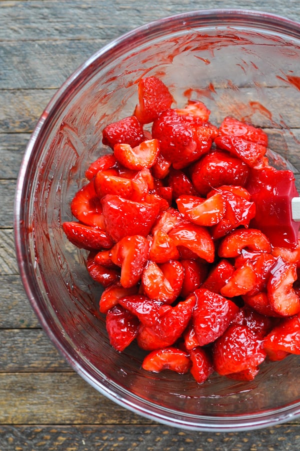 An overhead image of sliced strawberries in a glass bowl, coated in a sweet and shiny strawberry glaze.