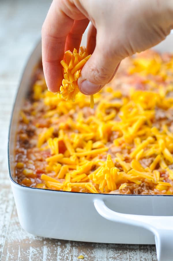 Sprinkling grated cheese on top of taco casserole with rice