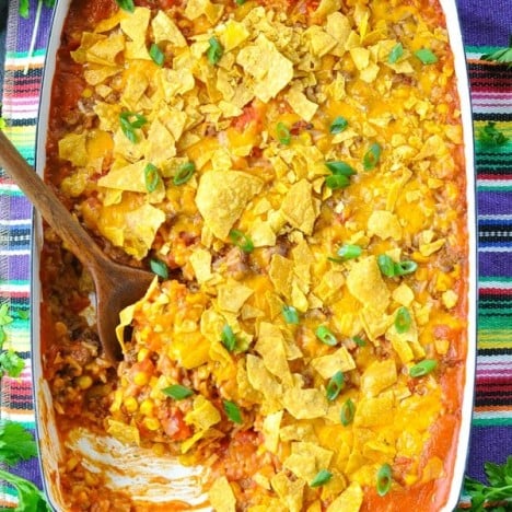 Overhead shot of taco casserole with rice in a white baking dish with a wooden serving spoon