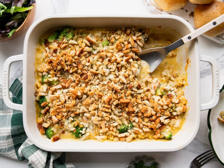 Horizontal overhead image of a serving spoon in a white dish full of chicken broccoli pasta casserole.