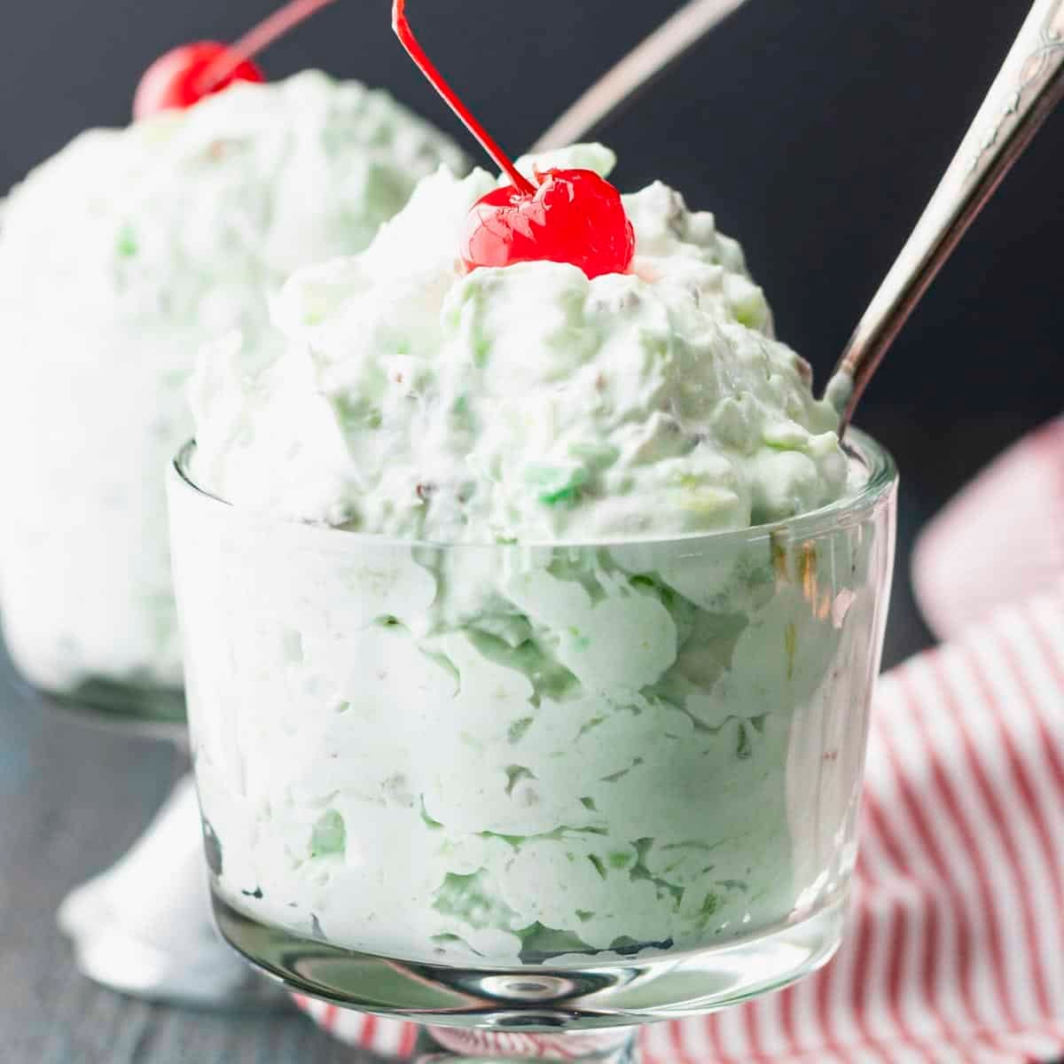 Close up square side shot of a Watergate salad recipe with a cherry on top.