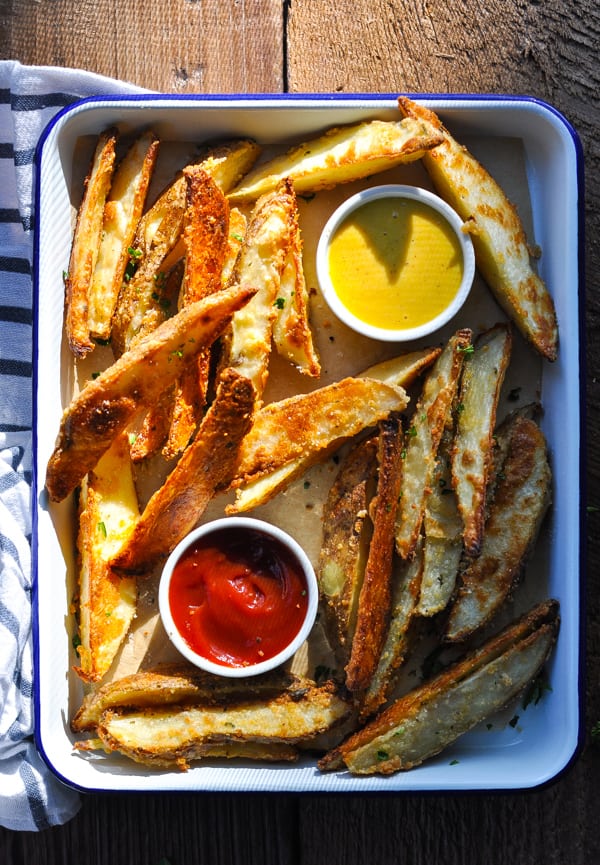 Overhead shot of baked potato wedges on a tray with a striped towel nearby