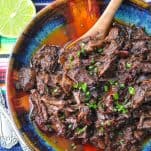 Close overhead shot of beef barbacoa in a bowl with a wooden serving spoon