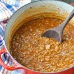 Ranch style beans in a red dutch oven with a wooden spoon
