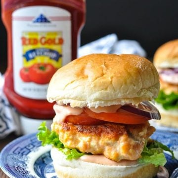 Close up front shot of a salmon burger on a bun with toppings and sauce
