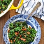 Bowl and skillet with sauteed kale on a wooden table