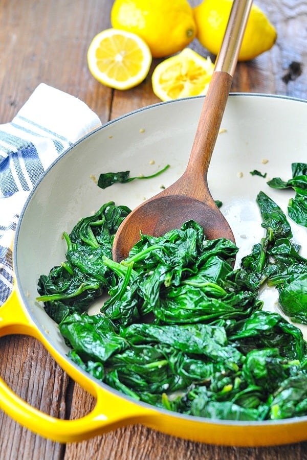 Front shot of sauteed spinach with garlic in a yellow cast iron skillet with a wooden spoon