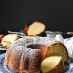 Front image of a sour cream pound cake with powdered sugar on top in front of a black background