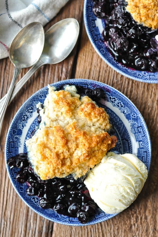 Overhead shot of blueberry cobbler on blue and white plates on a wooden table