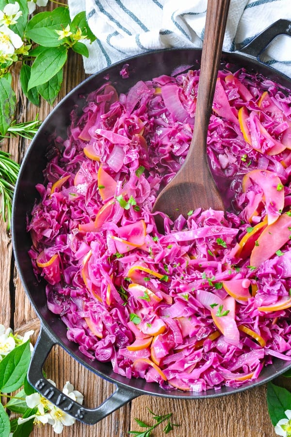 Overhead shot of a wooden spoon stirring braised red cabbage in a skillet