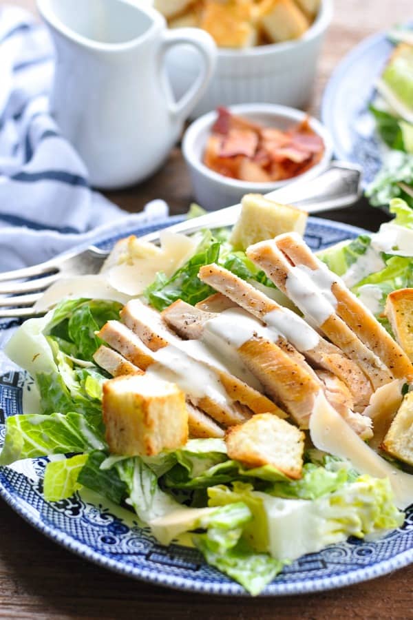 Close up shot of sliced chicken breast served on top of a caesar salad with croutons and dressing