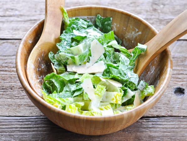 Caesar salad in a large wooden bowl topped with shaved parmesan cheese
