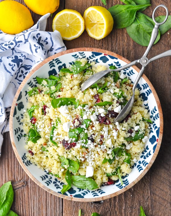 Overhead shot of a bowl of couscous salad with cranberries surrounded by lemons and spinach