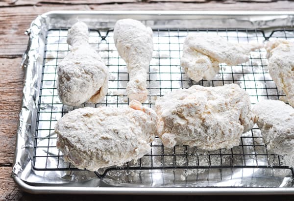 Chicken coated with flour drying on a wire rack