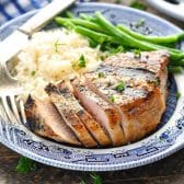 Close up square side shot of grilled pork chops on a blue and white plate.