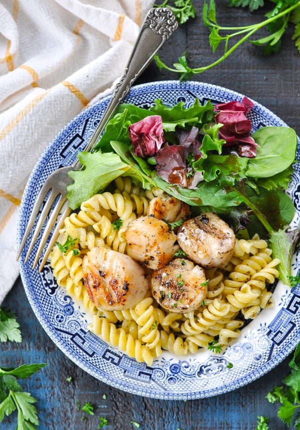 Overhead image of grilled scallops served over pasta with a side salad