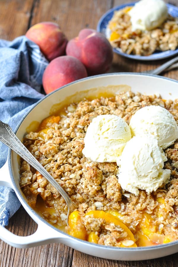 Close up side shot of an old fashioned peach crisp recipe baked in a white cast iron skillet