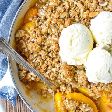 Close overhead image of spoon scooping up peach crisp with three scoops of vanilla ice cream on top