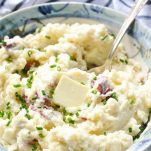 Close up side shot of a bowl of mashed red potatoes with skin and chives on top