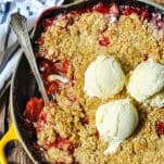 Close overhead shot of three scoops of vanilla ice cream on top of a strawberry crisp in a cast iron skillet
