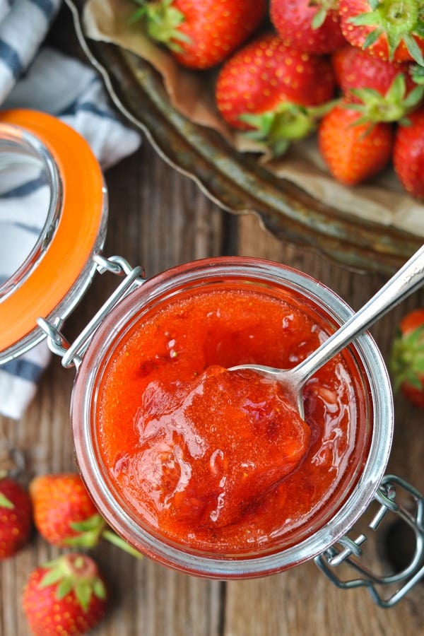 Overhead image of a spoon scooping up strawberry freezer jam from a glass jar