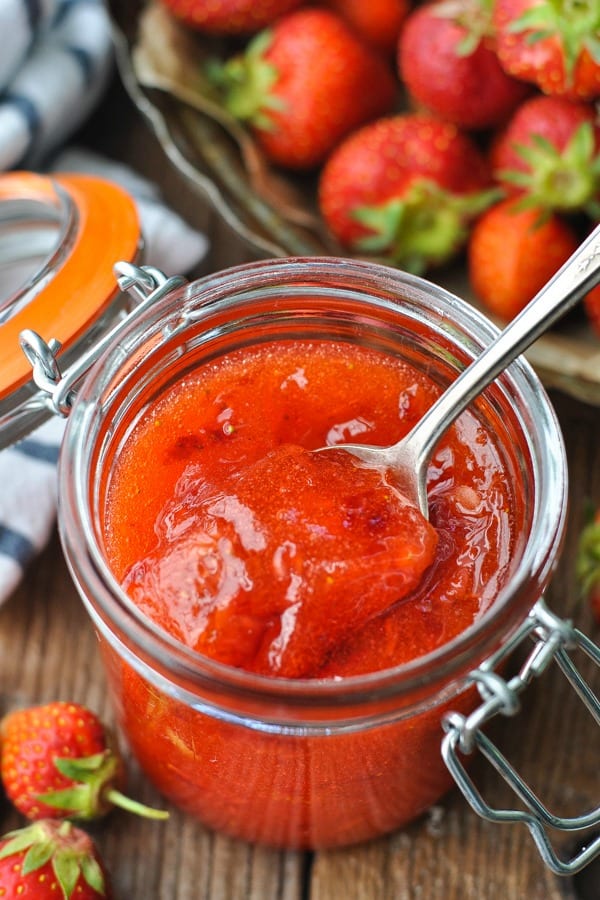 Side shot of a jar of strawberry freezer jam with a spoon inside