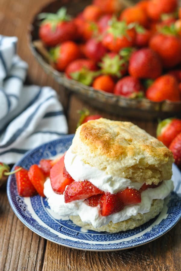 Side shot of a plate of strawberry shortcake recipe with a bowl of berries on the wooden table
