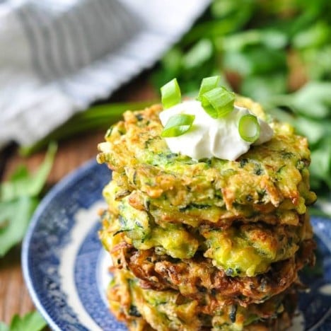 Four zucchini fritters stacked on a blue and white plate