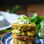 Sour cream and green onions on top of a stack of zucchini fritters