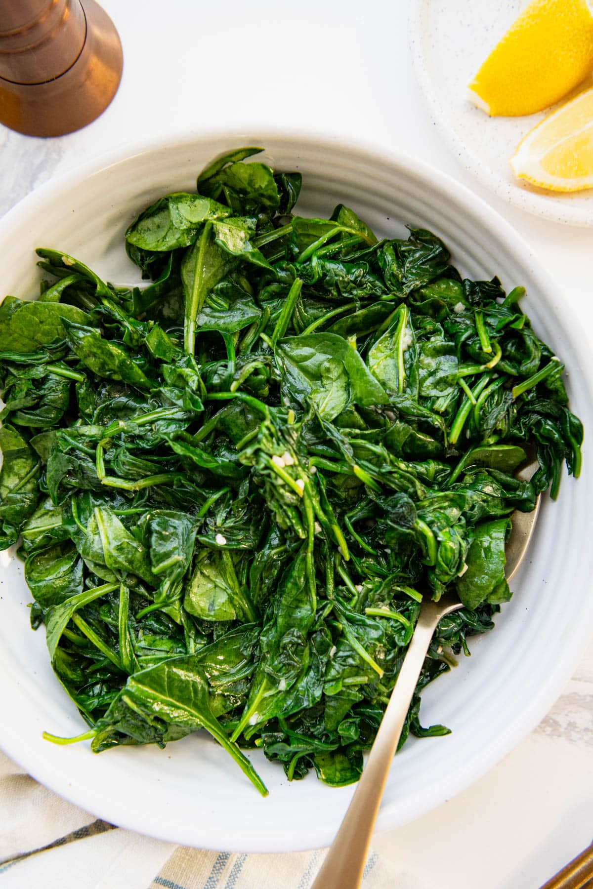 Close overhead shot of a white bowl full of sauteed spinach with garlic and lemon.