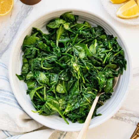 Square overhead shot of sauteed spinach with garlic and lemon in a white bowl.