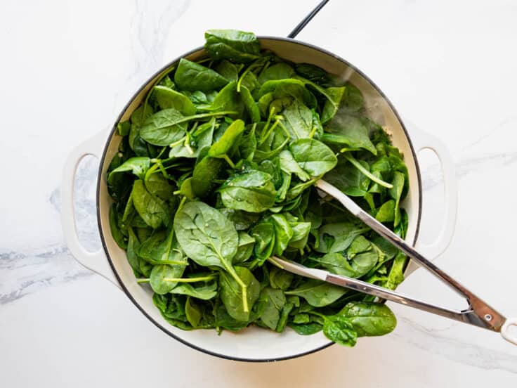 Adding fresh spinach leaves to a pan.