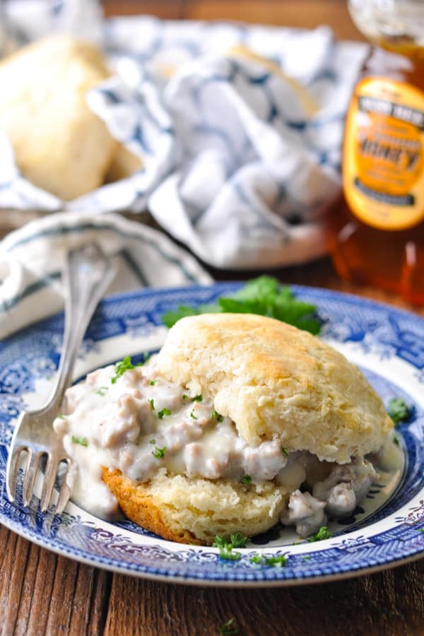 A buttermilk biscuit on a blue and white plate served with a creamy sausage gravy