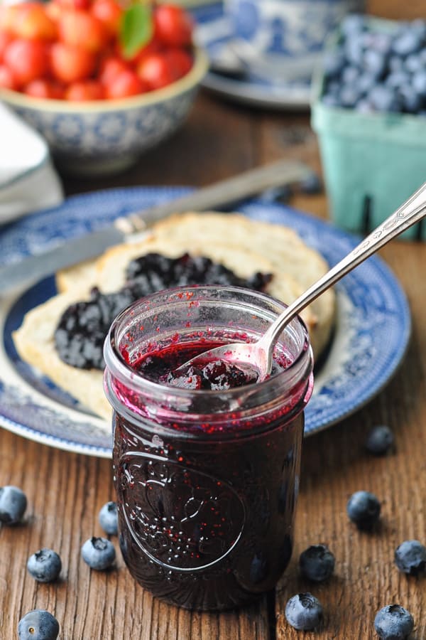Front shot of homemade blueberry jam in a jar on a wooden table with toast in the background