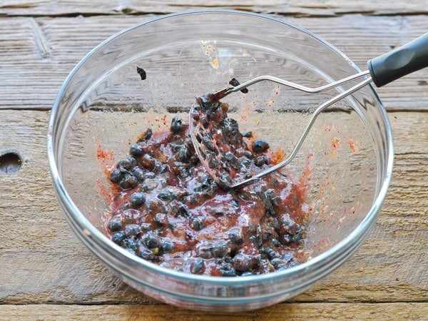 Using a potato masher to mash fresh blueberries in a big glass bowl