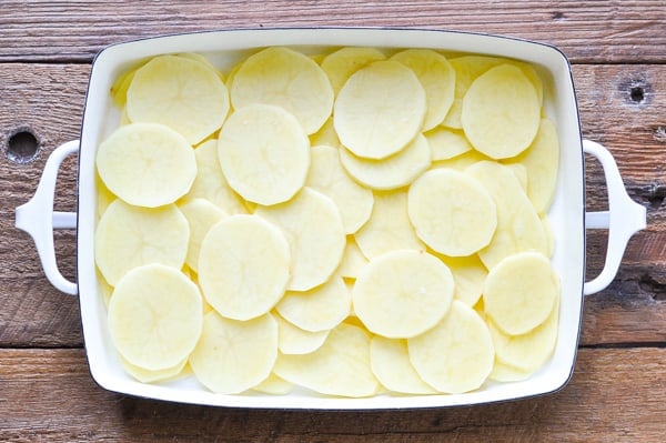 Sliced potatoes layered in the bottom of a casserole dish