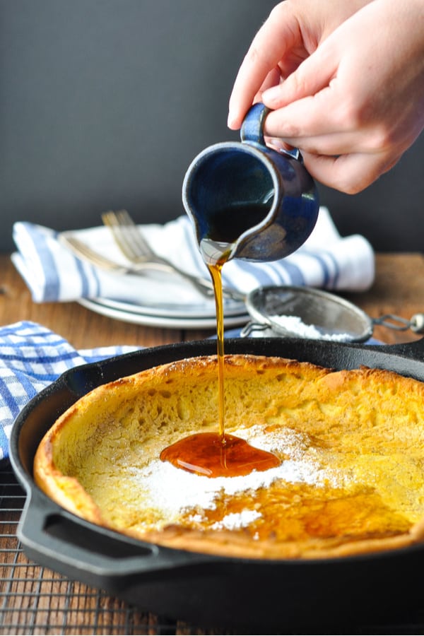 Front shot of child's hands pouring maple syrup on a Dutch Baby Pancake