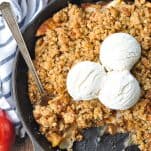 Close overhead shot of easy apple crisp in a cast iron skillet with three scoops of vanilla ice ream