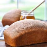 Front shot of two loaves of homemade wheat bread on a cutting board in front of a window