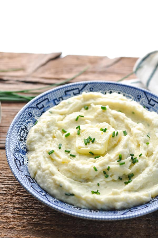 Bowl of cauliflower mash topped with fresh chives in a blue and white bowl