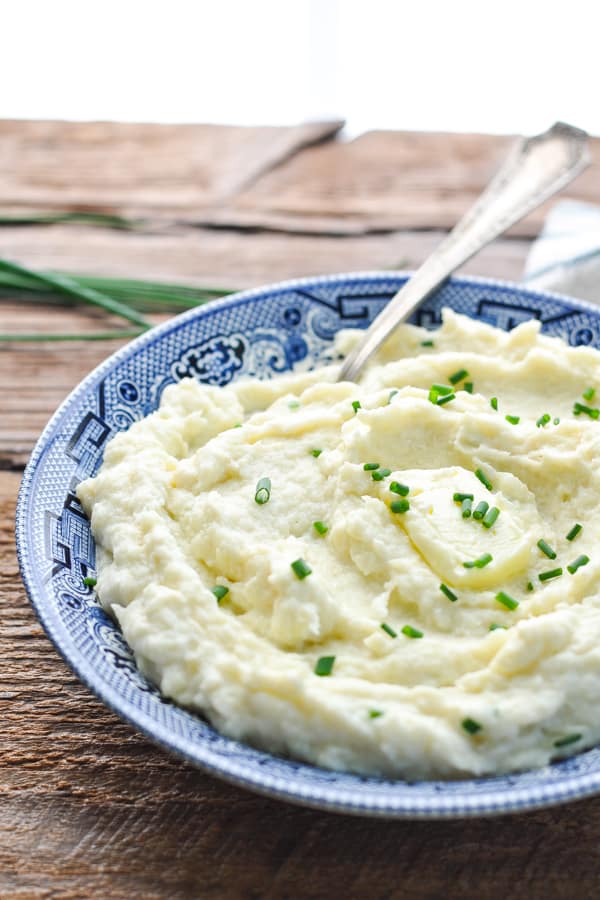 Close up side shot of a bowl of garlic cauliflower mash with a pat of butter and chives on top