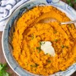An easy mashed sweet potatoes recipe served in a ceramic bowl and garnished with butter and herbs