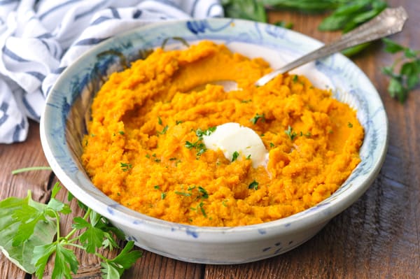 Close up horizontal shot of a bowl of mashed sweet potatoes with a pat of butter on top