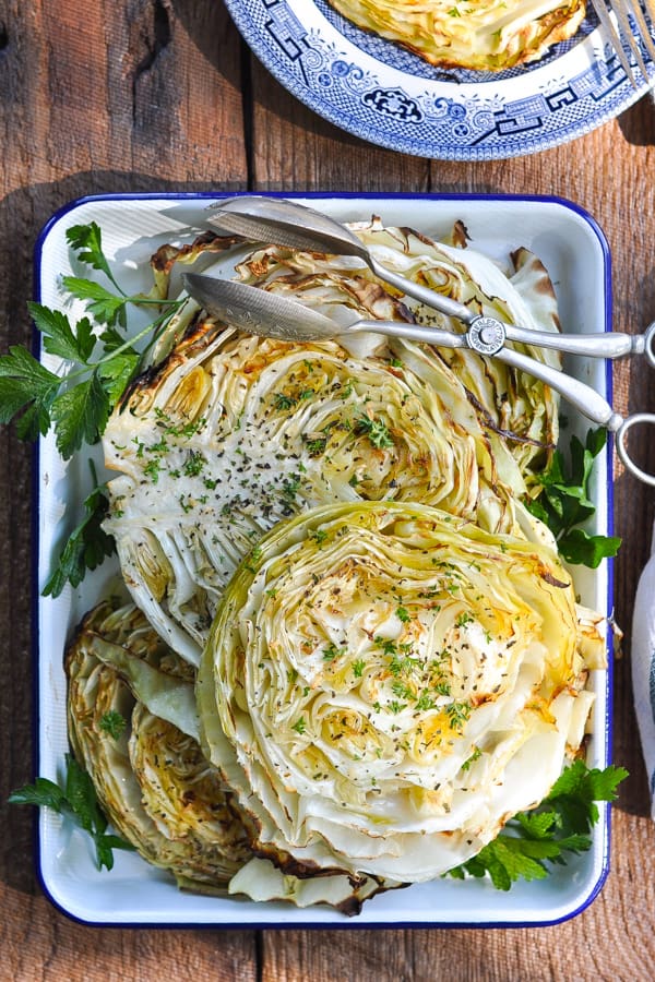 Overhead image of a blue and white tray full of roasted cabbage steaks