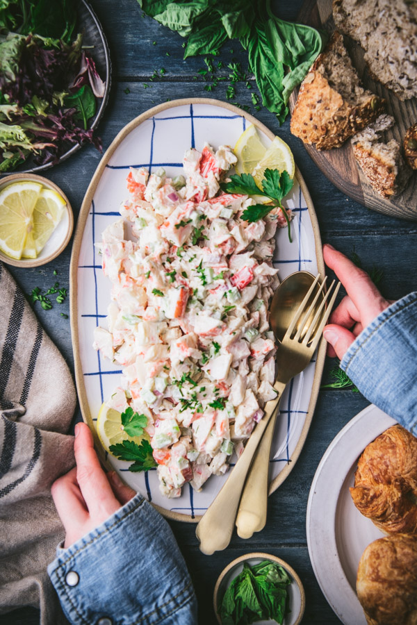 Overhead shot of hands holding a platter of seafood salad with bread on the side